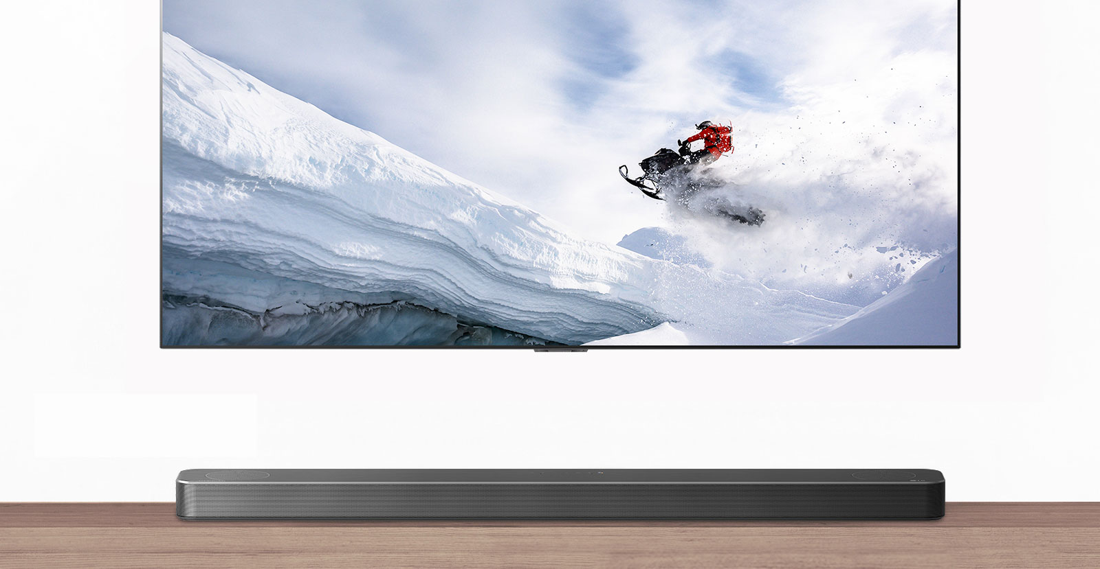 TV og lydplanke vist forfra. TV viser en mann som rir på en snøskuter i snøkledde fjell. HDMI 2.1-logoen vises under TVen. 