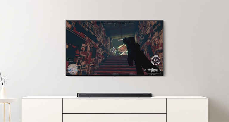 Det er TV og lydplanke i en stue. Et FPS-spill vises på en TV-skjerm og TV-kanalen byttes til et fotballspill.