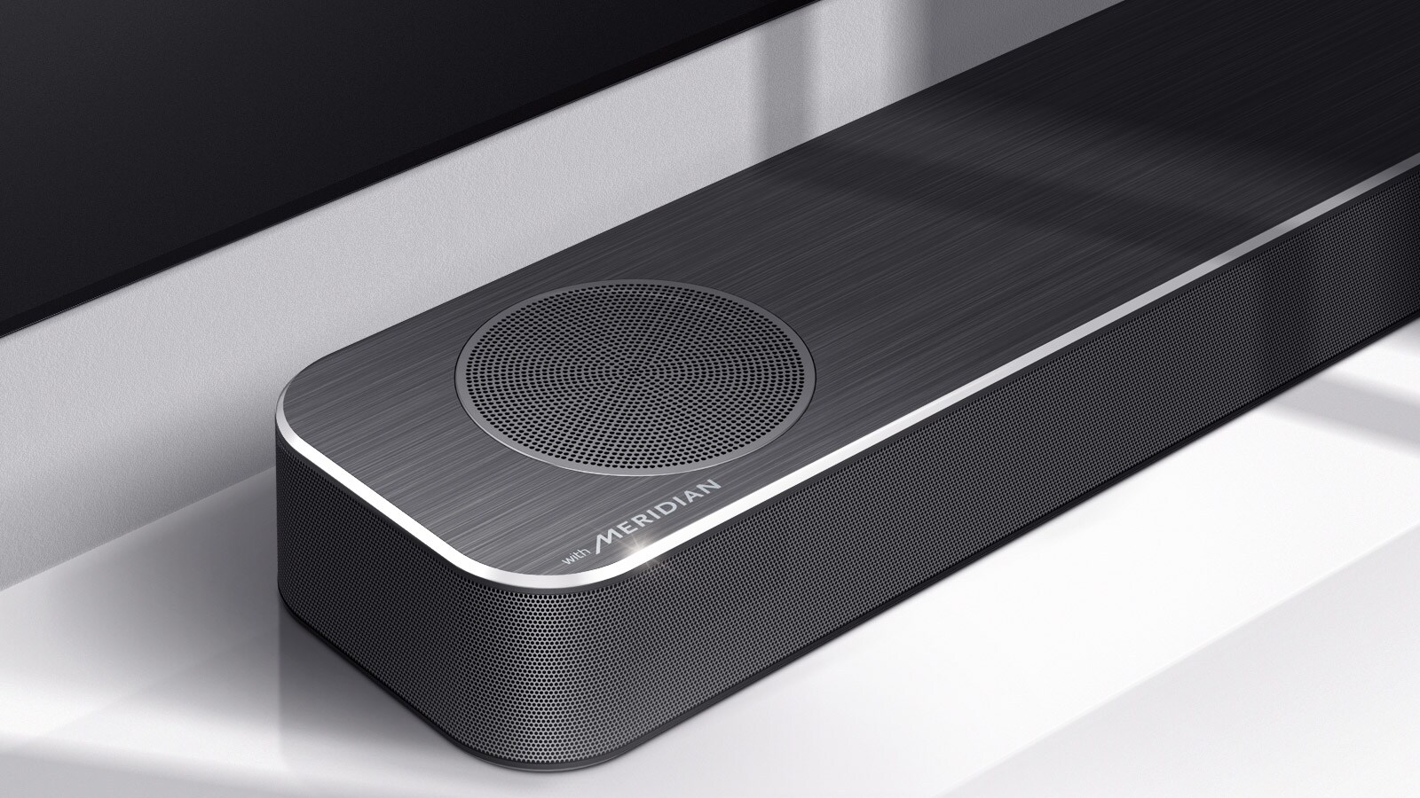 Nærbilde av LG Soundbars venstre side med Meridian-logoen vist på nedre venstre hjørne av produktet. Nedre venstre side av TVen er også synlig.
