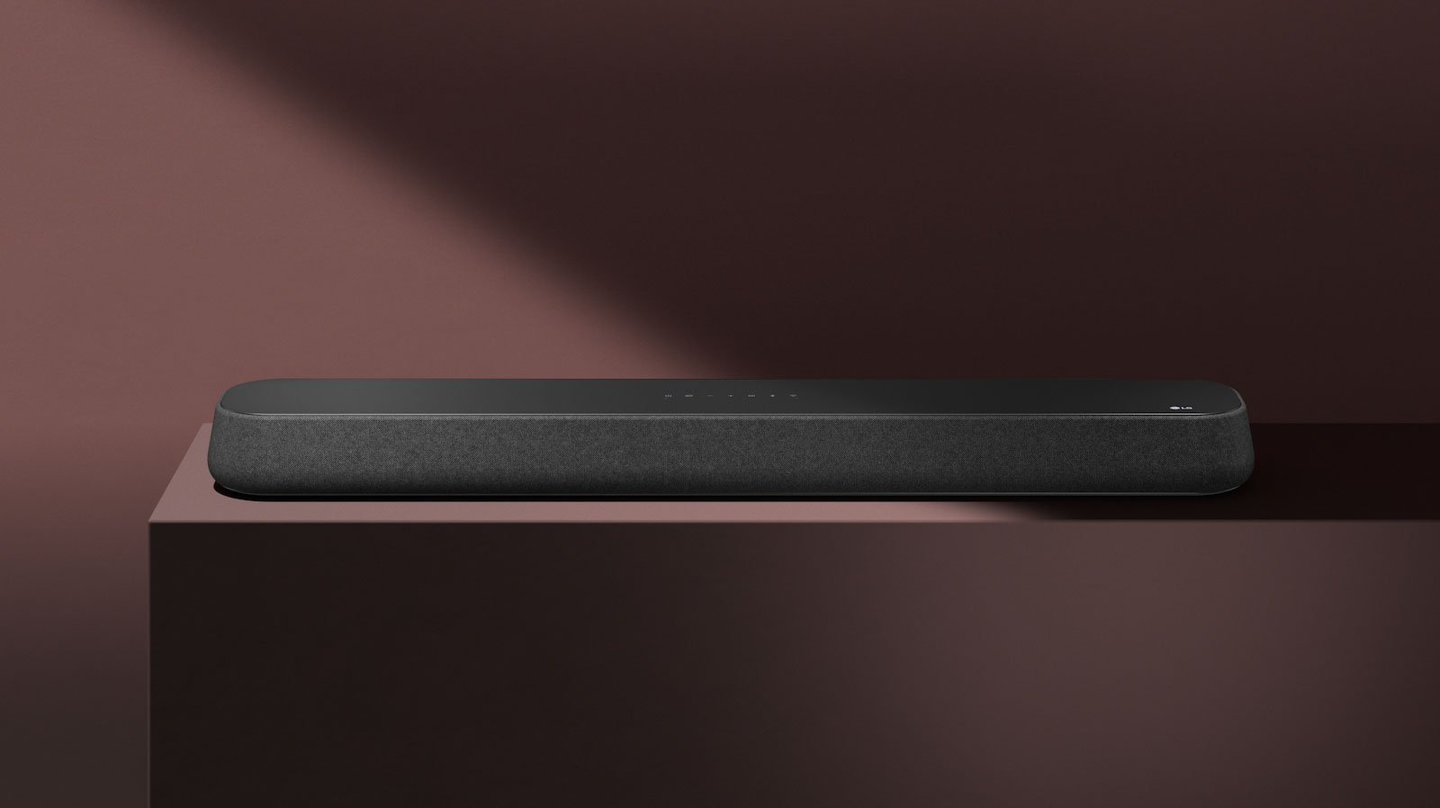 LG Sound Bar SE6S er plassert på den røde boksen foran rød bakgrunn. En svart skygge dekker øvre høyre halvdel av bildet.