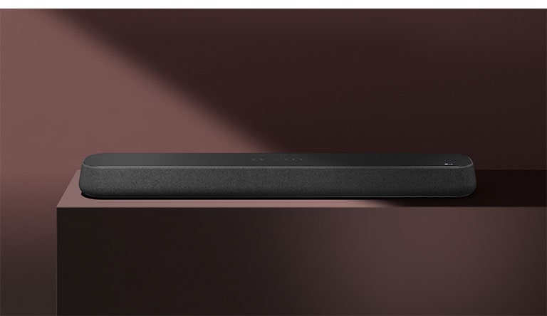 LG Sound Bar SE6S er plassert på den røde boksen foran rød bakgrunn. En svart skygge dekker øvre høyre halvdel av bildet.