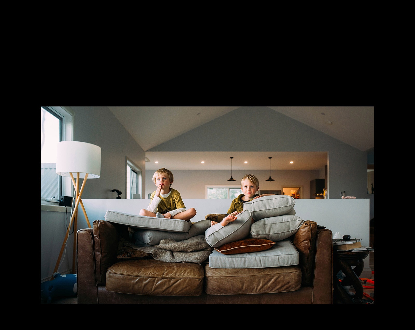 To tvillinggutter sitter på en sofa og ser på noe.