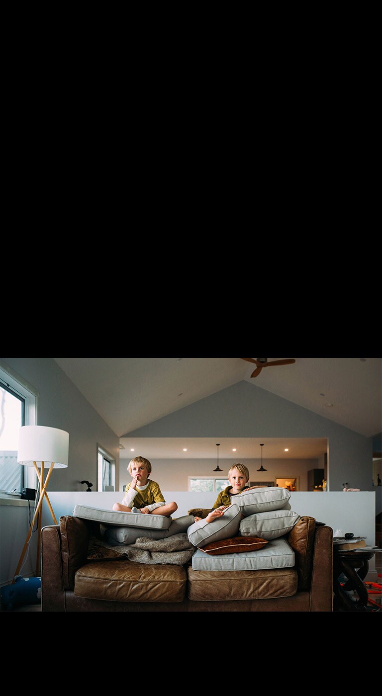 To tvillinggutter sitter på en sofa og ser på noe.