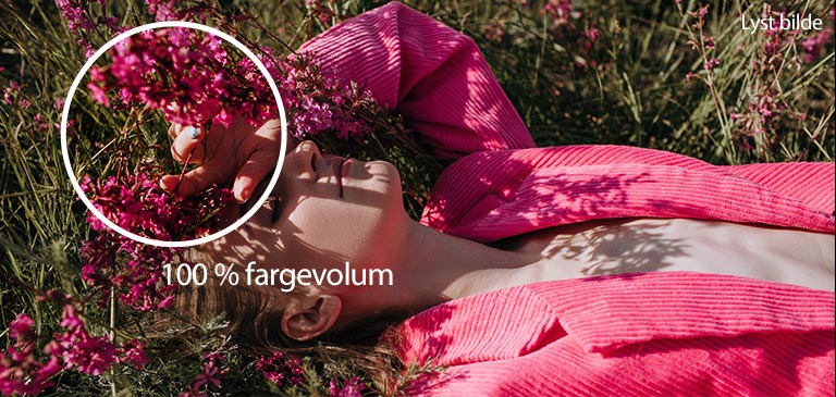 Video som viser en ung jente som holder en hånd over øynene liggende på en gresseng med rosa blomster. Etter hvert som videoen spilles av, blir fargene rikere og prosentdelsindikatoren for fargevolum øker fra 70 % til 100 %.