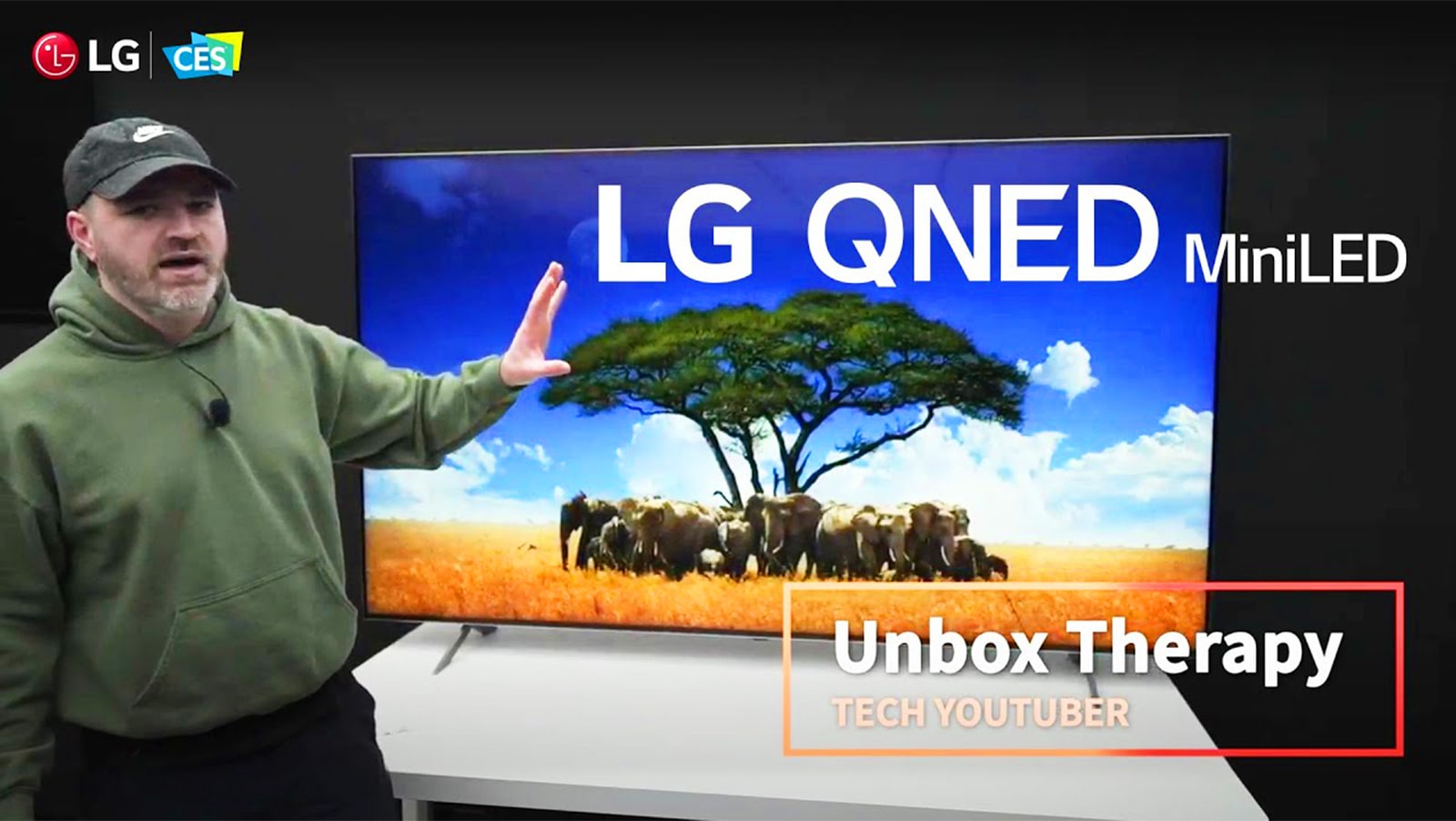 Youtuberen Unbox Therapy står foran en LG QNED MiniLED TV. Skjermen viser et bilde av en elefantflokk som omkranser et tre.