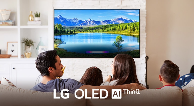 En familie i en lys stue som ser på et landskap som vises på en veggmontert TV