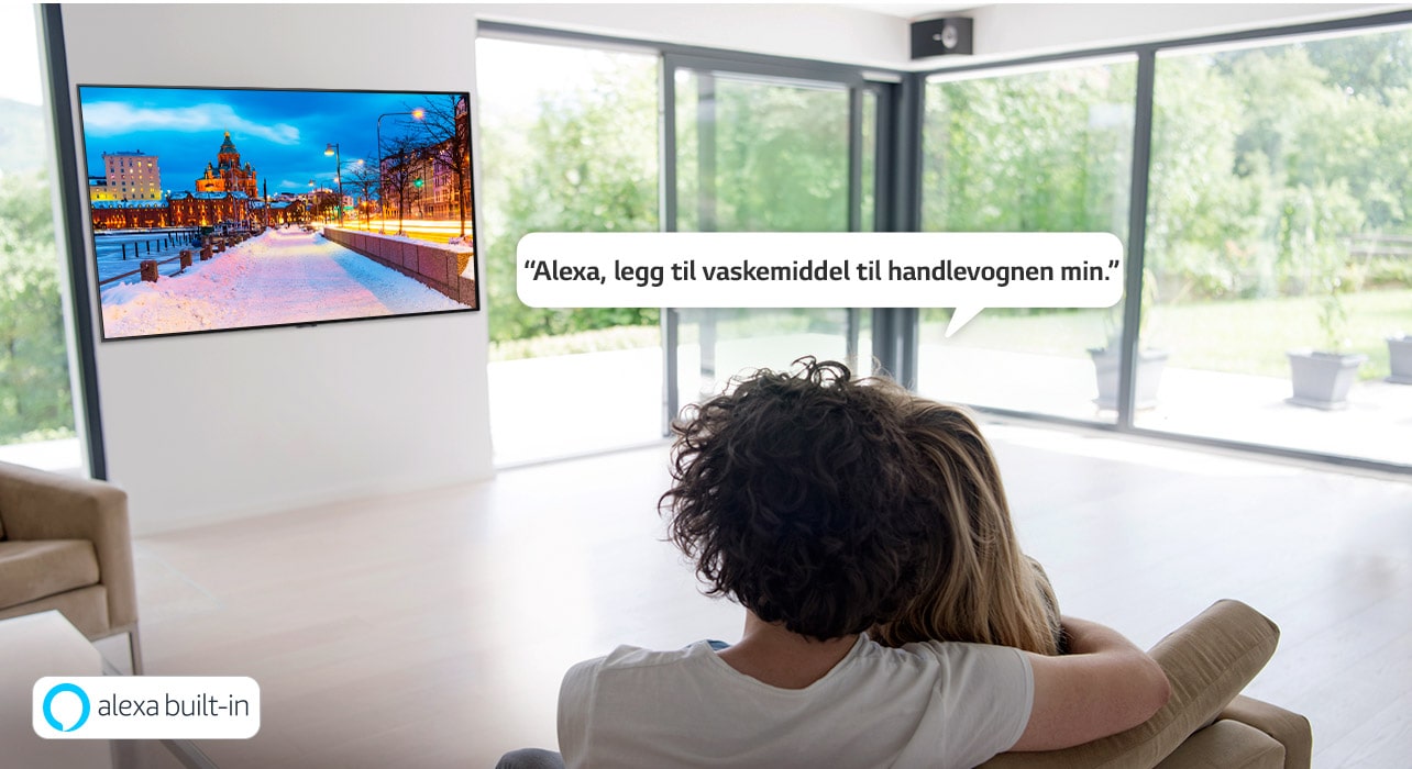 Et par sitter på en sofa og spør Amazon Alexa om å legge til vaskemiddel til handlevognen