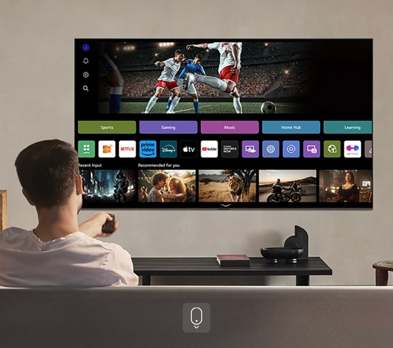 Person på sofaen som strekker ut en fjernkontroll. LG AI TV på veggen med LG webOS på skjermen.