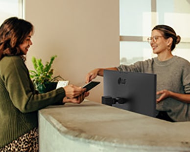 Vennlig resepsjonist som viser en kvinne hvor hun skal signere på et digitalt nettbrett.