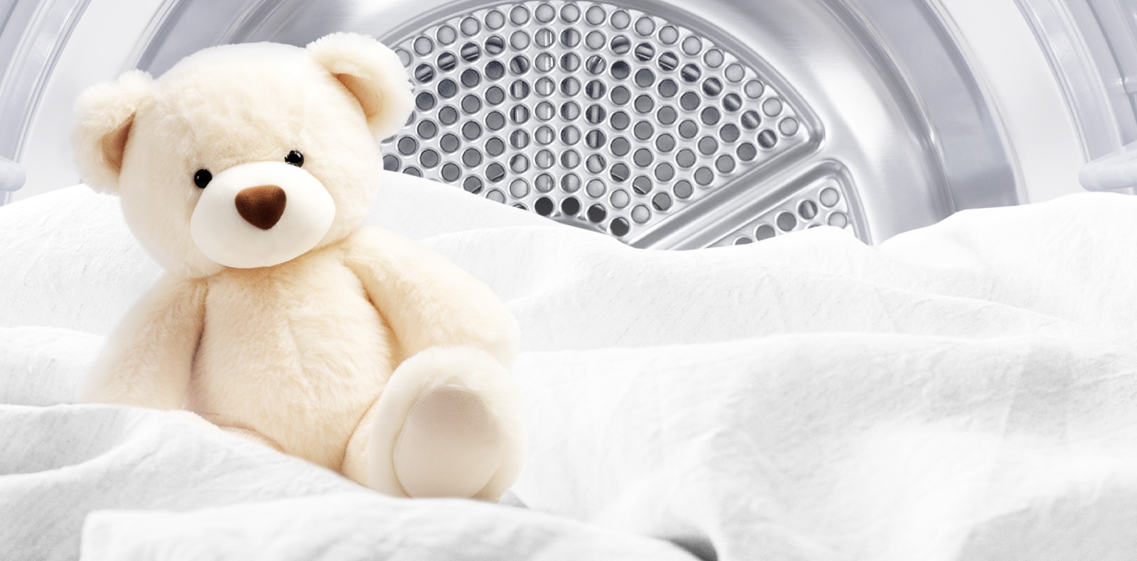 Bilde av en ren bamse og hvitt stoff inne i en tørketrommel.