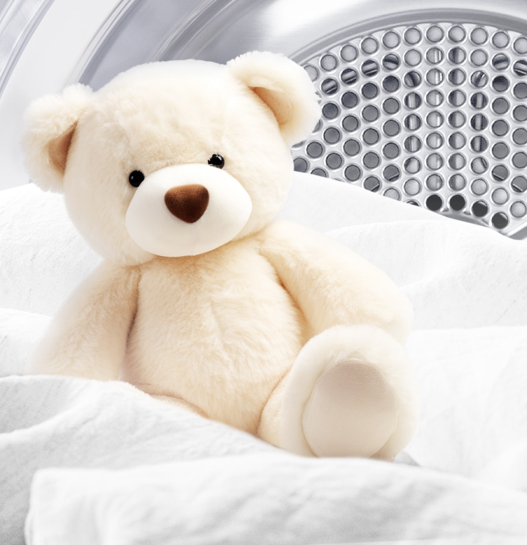 Bilde av en ren bamse og hvitt stoff inne i en tørketrommel.