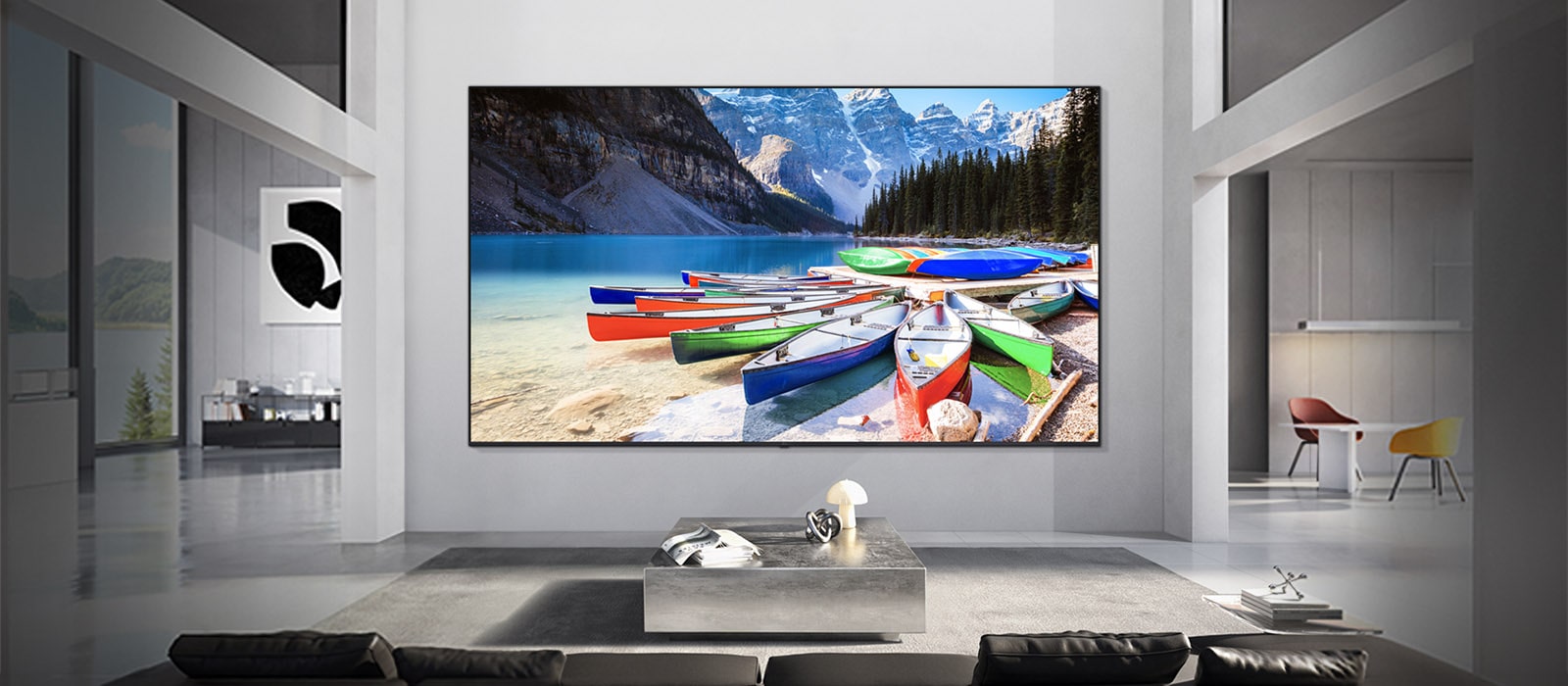 LG TV er veggmontert i et moderne oppholdsrom, der skjermen viser en levende innsjøscene med fargerike båter og fjell, som illustrerer hvordan skjermstørrelsen passer til rommet og skaper en balansert og oppslukende seeropplevelse.