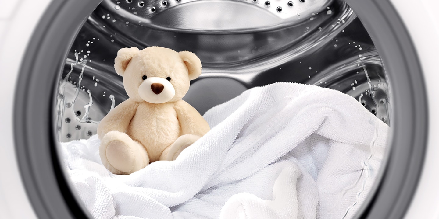 Et kosedyr og et teppe inne i vaskemaskintrommelen mens vasken pågår