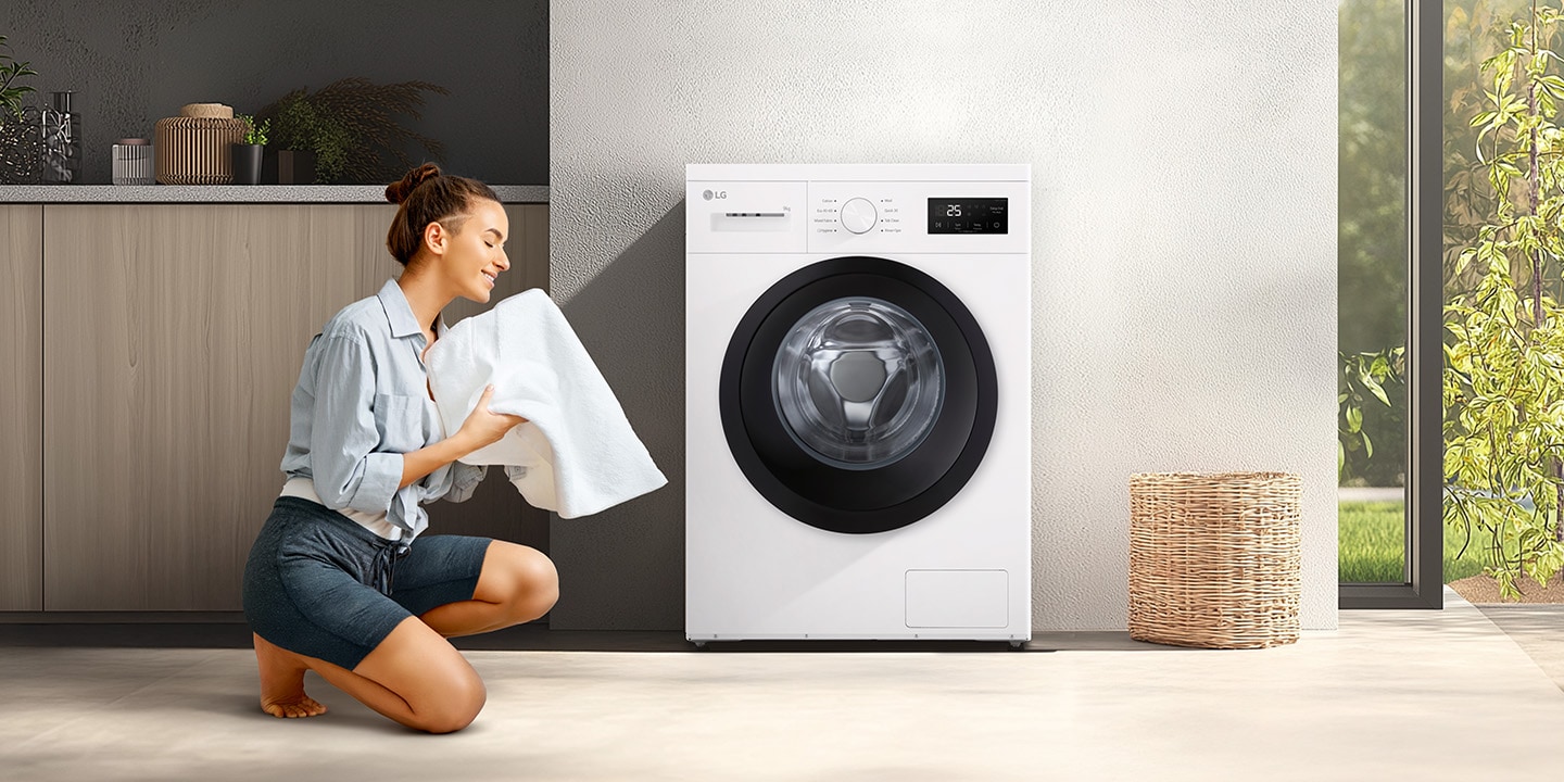 En kvinne som kneler foran en vaskemaskin i stuen og holder et rent teppe