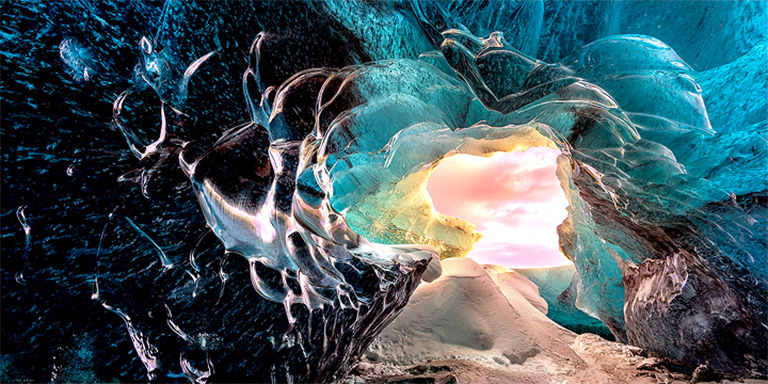 Perspective from a cave interior, looking out towards the entrance. The cave is surreal-looking with highly detailed rock and crystal formations. The scene highlights the visually lossless picture quality on LG True Wireless TVs.