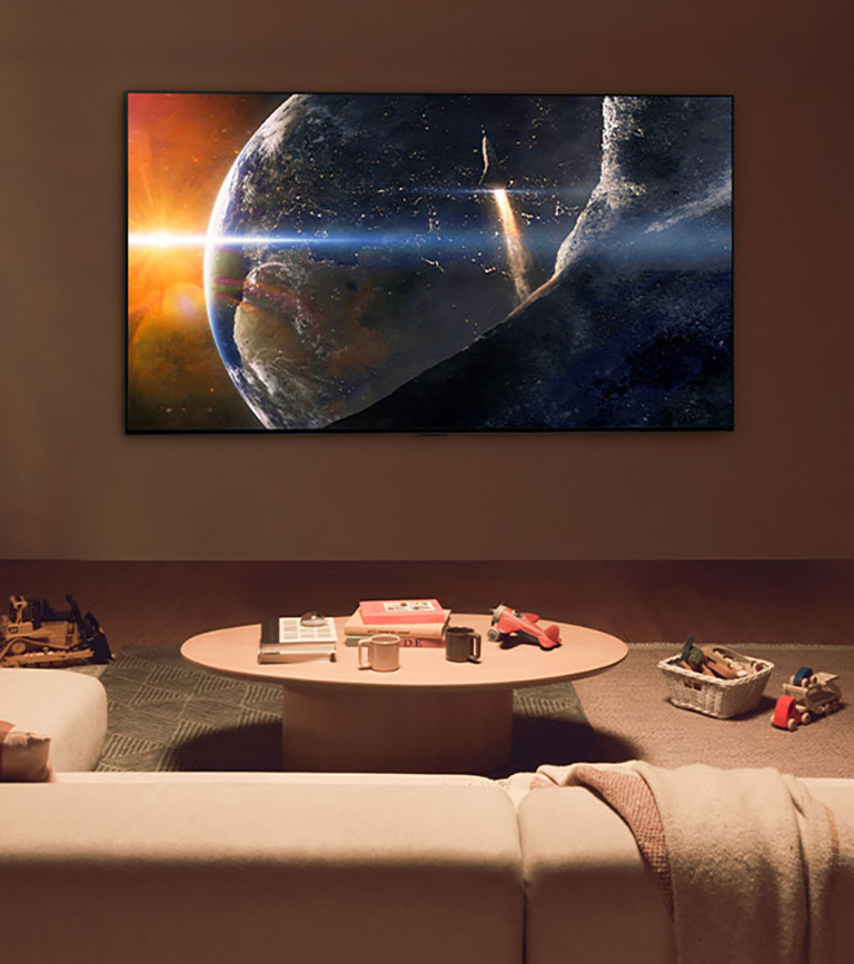 An image of a family sat on the floor of a low-lit living room by a small table, looking up at an LG TV mounted on the wall showing the Earth from space.
