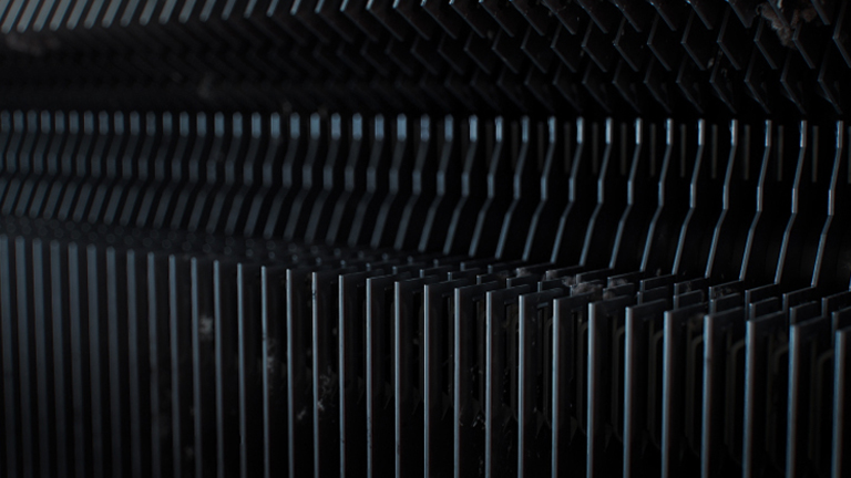 Close-up view of dusty metal heat exchanger fins inside an air conditioner with a pause icon overlay.