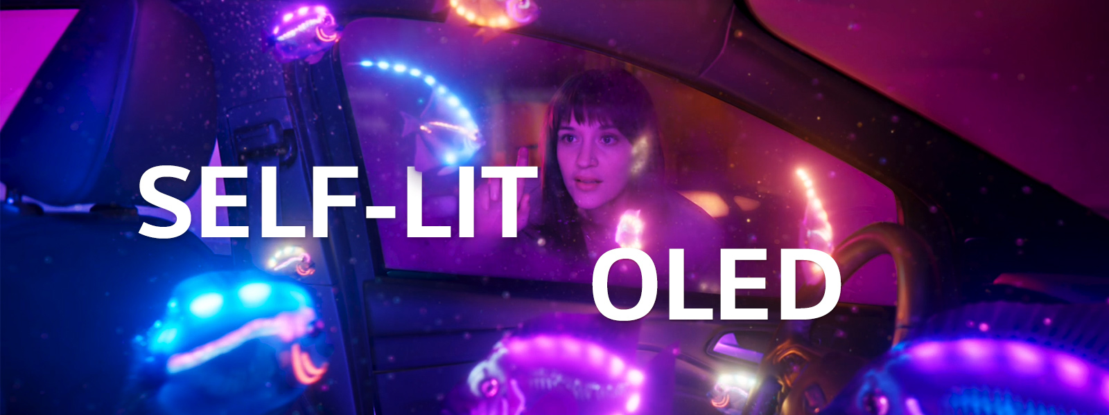 A woman watching inside of a car filled with shiny fish in multiple colors. And, there is the text of ‘SELF-LIT OLED’ in the middle of the image.