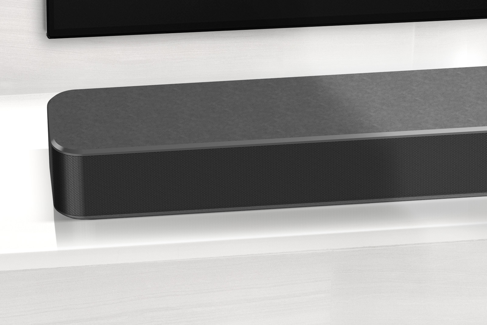 Close-up of LG Soundbar left corner. Bottom left side of TV is also visible. 