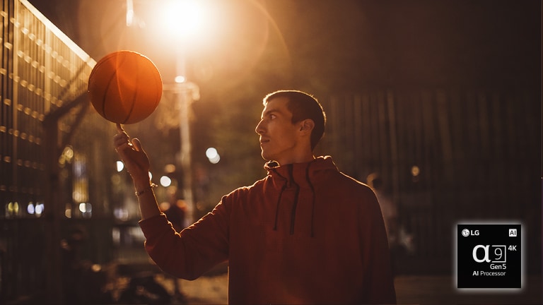 A man in a basketball court at night spins a basketball on his finger.
