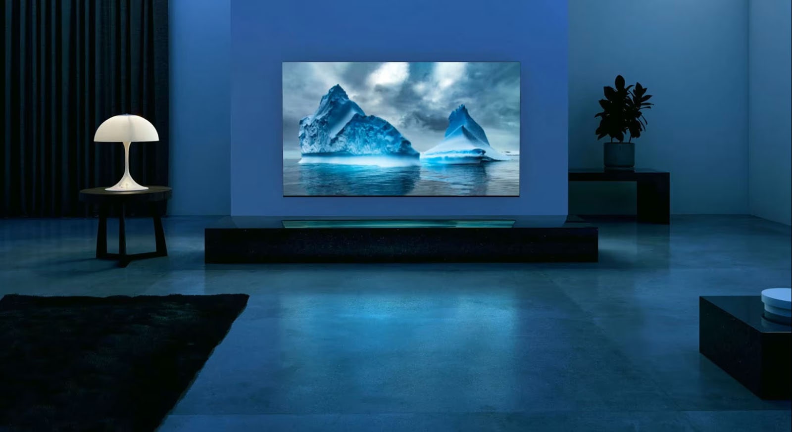 Niebieski neonowy obwód porusza się dookoła na zdjęciu niebieskiego lodowca. Kamera oddala się, aby ukazać ten niebieski lodowiec na ekranie telewizora. Telewizor znajduje się w szerokim pokoju dziennym z niebieskim tłem. 