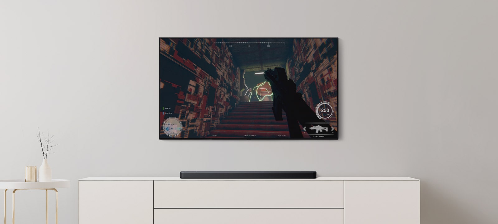 W salonie znajduje się telewizor i soundbar. Na ekranie telewizora wyświetlana jest gra FPS, a po przełączeniu kanału gra w piłkę nożną (odtwarzanie materiału wideo).