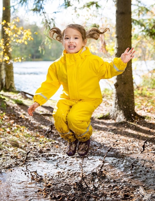A girl is jumping in a mud puddle.