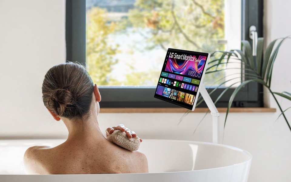 A woman looking at an LG 360 monitor while taking a half-bath in a bathtub.