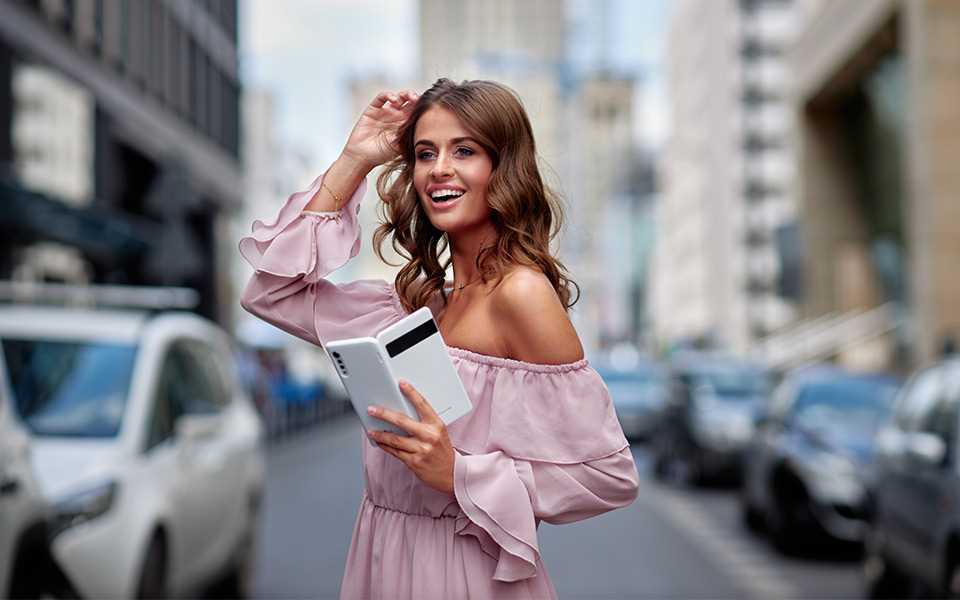 A woman is standing on the street holding an LG VELVET smartphone with Dual Screen in her hand.