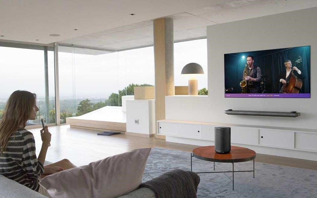 Kobieta siedząca w swoim salonie, za pomocą pilota LG, rozmawia z jej telewizorem LG OLED W8.