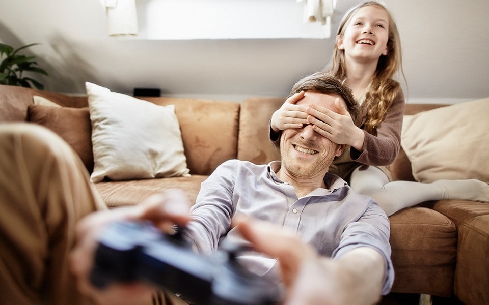 A man trying to playing a video game whilst a child covers his eyes