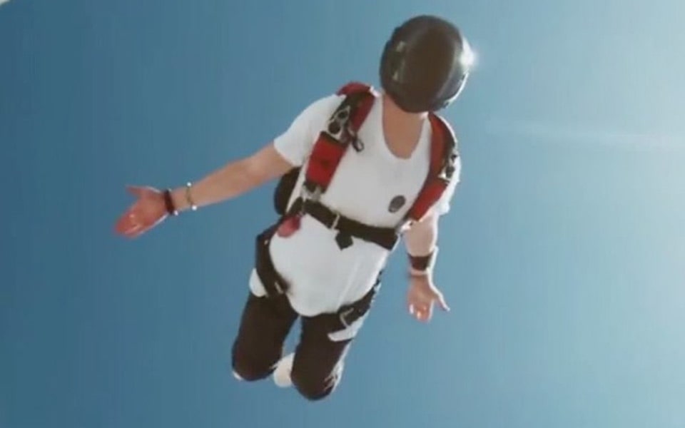 A man levitating in the sky whilst wearing a helmet and parachuting gear.