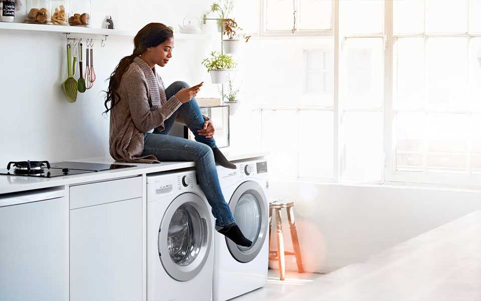 A woman on her phone whilst sitting on top of her LG washing machine and dryer.