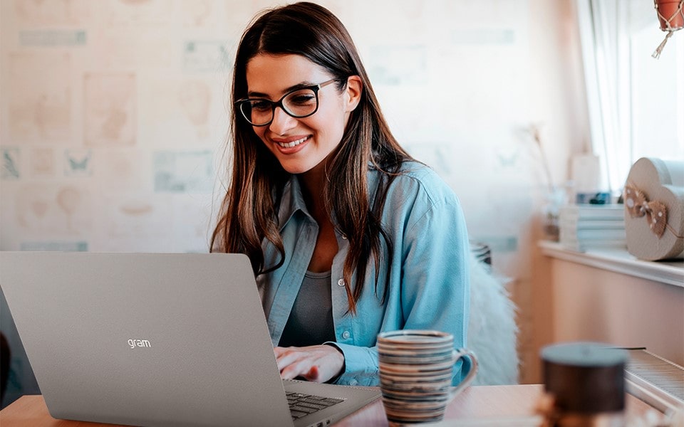 Uma mulher com óculos trabalha em uma mesa em seu laptop