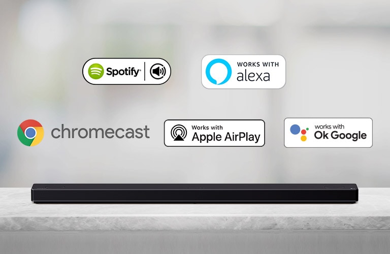 Există o bară de sunet amplasată pe o poliță gri și există sigle ale platformei AI, în ordinea Spotify, Chromecast, Apple Airplay și OK Google, de la stânga la dreapta.