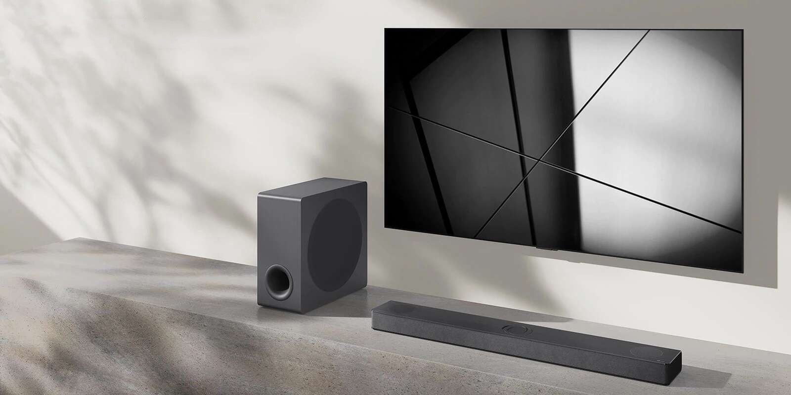 Egy LG S80QY hangprojektor és egy LG TV együtt egy nappaliban. A TV be van kapcsolva, és egy fekete-fehér kép látható rajta.