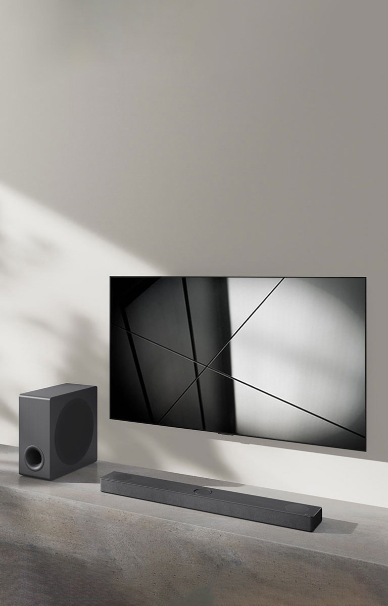 Egy LG S80QY hangprojektor és egy LG TV együtt egy nappaliban. A TV be van kapcsolva, és egy fekete-fehér kép látható rajta.