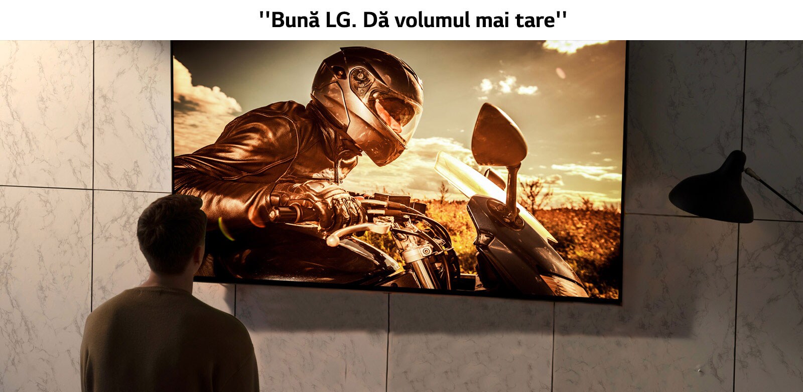 Perspectivă din spatele unui bărbat care se uită la televizorul de pe peretele din sufragerie. Pe ecran se vede o scenă cu o motocicletă dintr-un film.