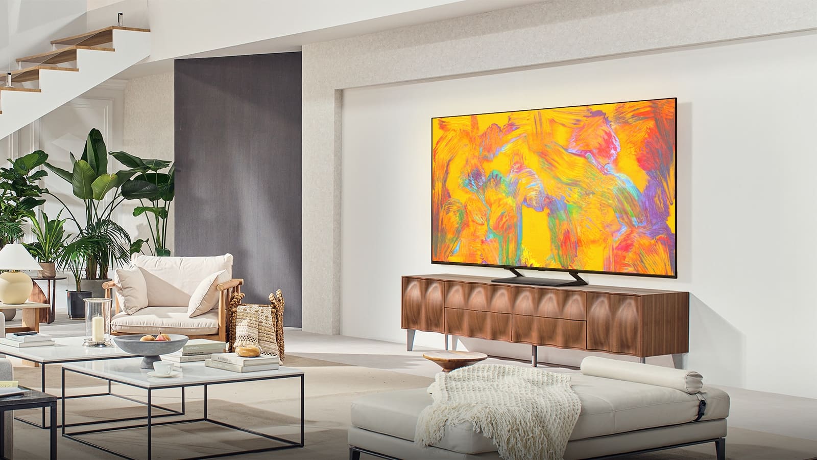 Televizorul LG QNED este așezat deasupra unui dulap pentru televizor într-un spațiu de living modern. Televizorul LG QNED afișează un fundal abstract în nuanțe de verde, roșu și portocaliu.