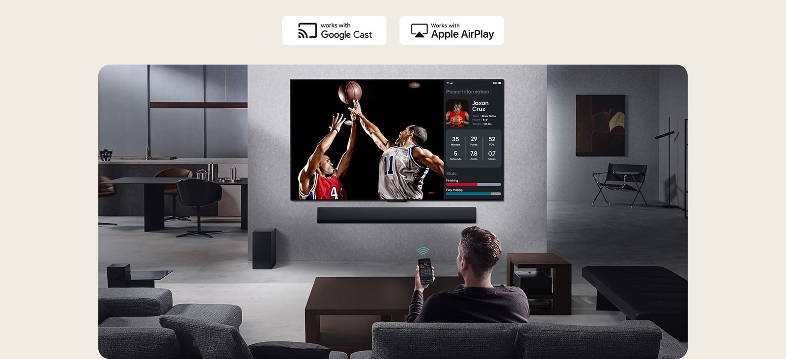 O persoană în livingul lor ținând telefonul. Pe telefon este un icon de transmitere care arată că ecranul telefonului este reflectat pe televizor. Pe televizor este un meci de baschet, iar pe lateral este ecranul reflectat, care arată statisticile jucătorilor.