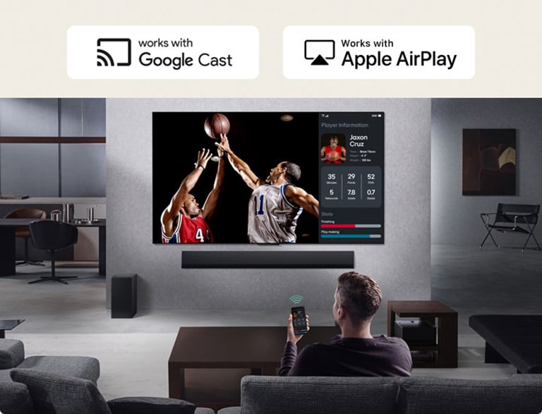 O persoană în livingul lor ținând telefonul. Pe telefon este un icon de transmitere care arată că ecranul telefonului este reflectat pe televizor. Pe televizor este un meci de baschet, iar pe lateral este ecranul reflectat, care arată statisticile jucătorilor.