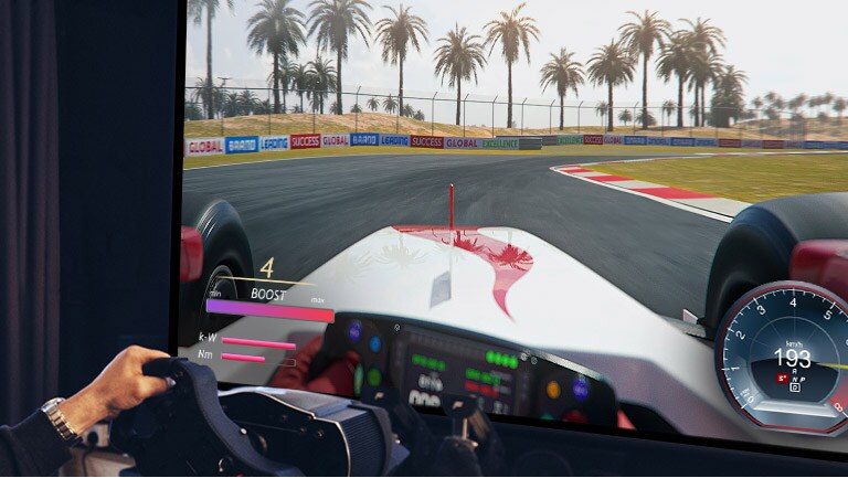 Prim-plan cu un jucător care are în mână un volan de curse în timpul unui joc de curse pe un ecran TV.