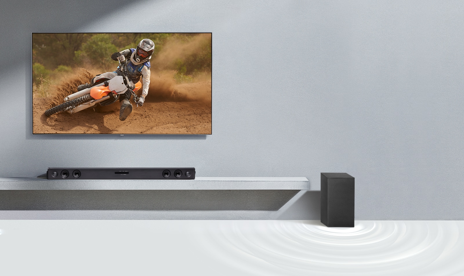 Bara de sunet SQC2 și televizorul LG sunt așezate împreună în camera de zi. Subwoofer-ul este așezat lângă bara de sunet. Televizorul este pornit și afișează o imagine cu o motocicletă.