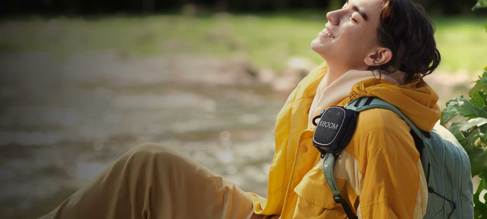 Un bărbat care stă pe podea și ascultă muzică cu LG XBOOM Go XG2T atârnat de rucsac.