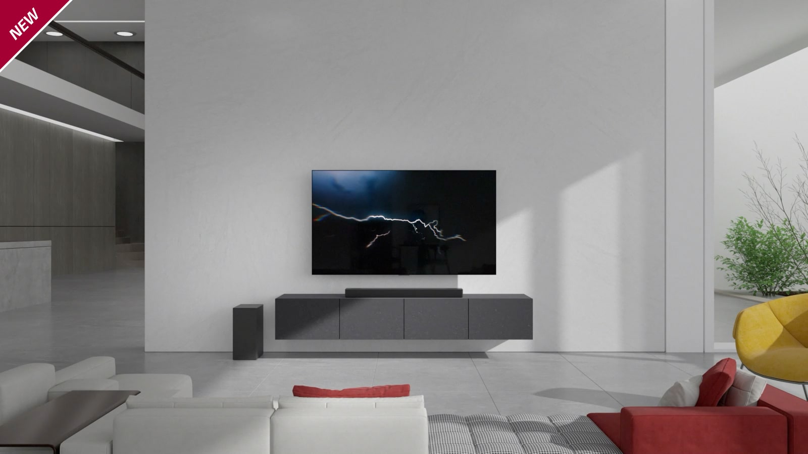 Bara de sunet este așezată pe dulapul gri cu un televizor agățat pe peretele din camera de zi. Un subwoofer wireless este așezat pe podea în partea stângă, iar lumina soarelui intră dinspre partea dreaptă a imaginii. O canapea lungă colorată în alb și roșu este așezată cu fața spre televizor și bara de sunet. Marcajul NEW (NOU) este afișat în colțul din stânga sus.
