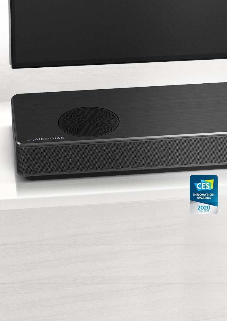 Prim-plan cu partea din stânga a soundbar LG, cu logo-ul Meridian afișat în colțul din stânga jos. Partea din stânga jos a televizorului este, de asemenea, vizibilă.