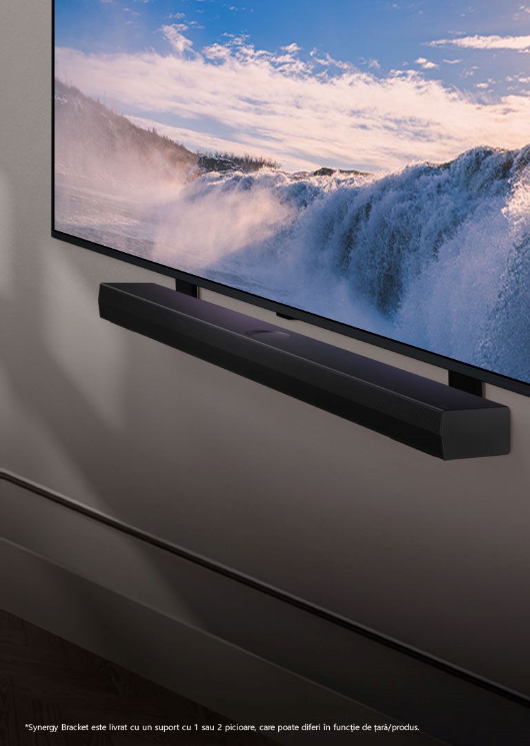 LG TV și soundbar sunt așezate într-o poziție înclinată, montate pe un perete. Pe televizor este afișat un prim plan al unei vaste cascade, iar lumina blândă a soarelui se îndreaptă peste perete, televizor și soundbar. O declinare a răspunderii transmite: „Suportul Synergy vine însoțit de un suport cu 1 pol sau 2 poli, care pot diferi în funcție de țară/produs.”