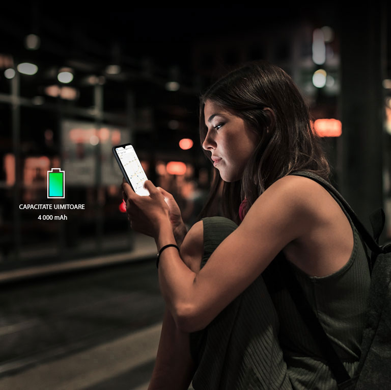 Femeie care caută pe internet de pe telefonul său, care mai are suficientă baterie, noapte târziu, într-o stație de metrou.