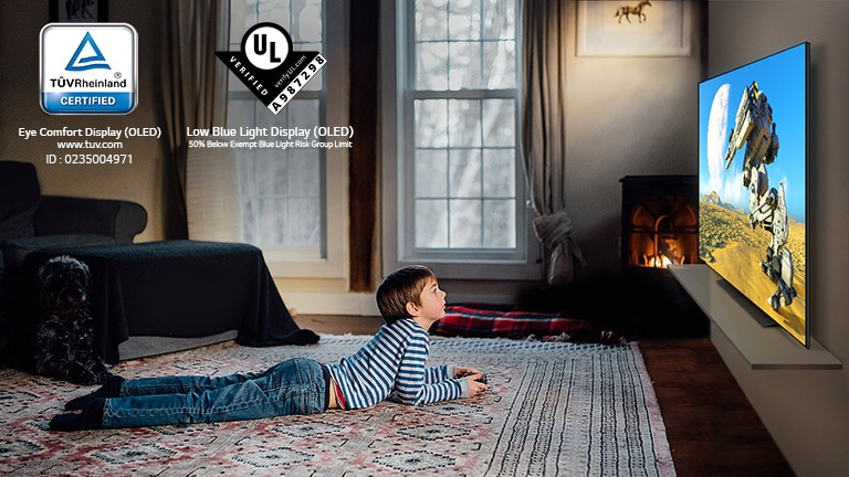 Copil care stă întins pe podea, ținând în mână o manșă de un joystick și joacă un joc pe un ecran TV