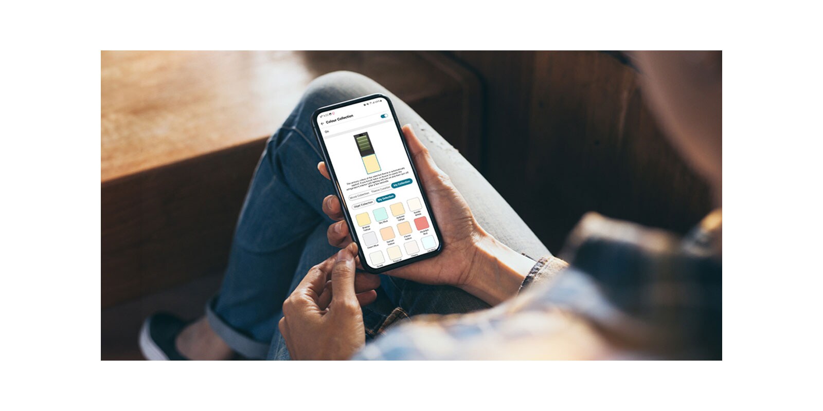 Na slici se vidi da neko proverava svoj mobilni telefon,  koji predstavlja dostupne boje LG InstaView sa MoodUP Donji zamrzivač frižidera u LG ThinQ aplikaciji.